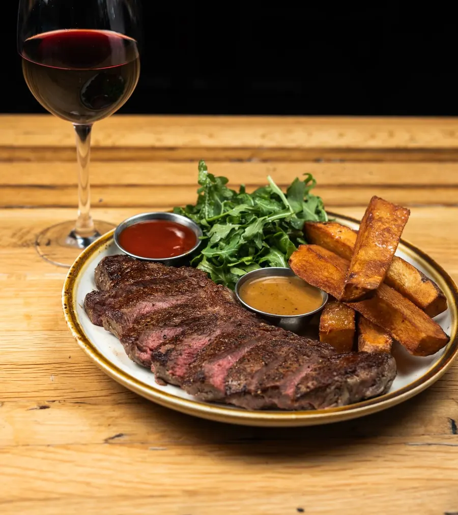 Sliced steak with fries and a glass of red wine