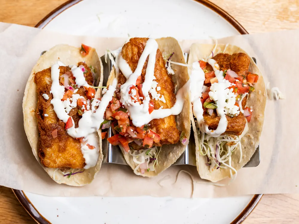 Three battered fish tacos with crema and pico de gallo, from above